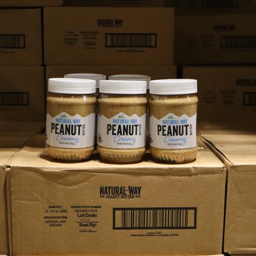 3 jars of  Natural Way creamy peanut butter on top of additional boxes of peanut butter