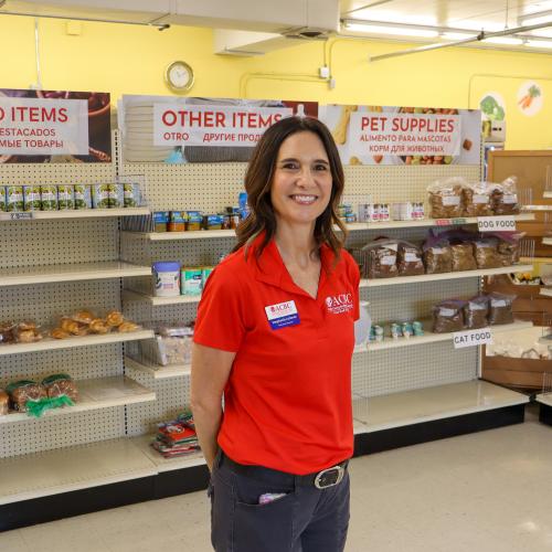 ACBC Food Shelf Executive Director Stephanie Lehman Stephanie Lehman, a brunette woman in a red shirt, stands in front of shelves of food