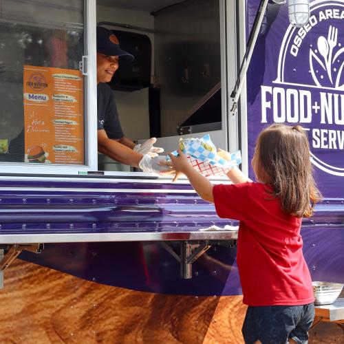 Osseo Area Schools Food Truck A child in a red shirt accepts a meal from a person through a food truck window