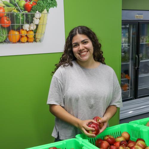 Rebeca, an intern at St. Peter Area Food Shelf Young woman in gray t-shirt smiling at the camera, holding apples