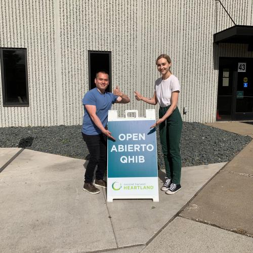 Two people stand beside an open sign with thumbs up