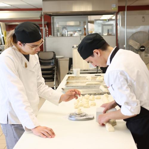 Two chefs cut bread dough in a kitchen