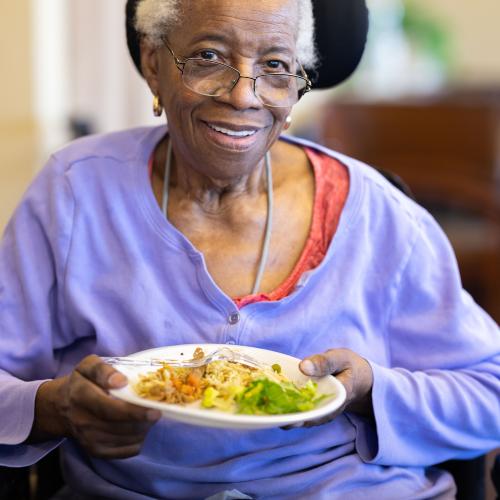 Elderly woman in wheelchair, enjoying a prepared meal 