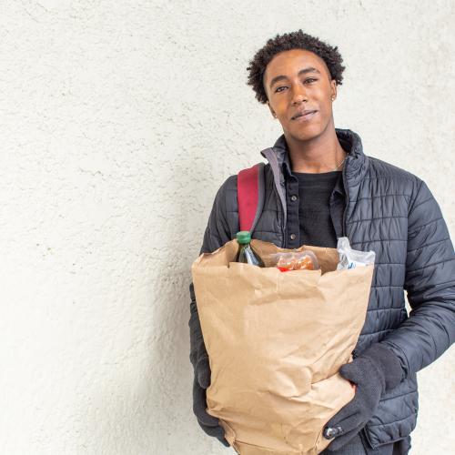 A person standing outside, holding a bag of groceries