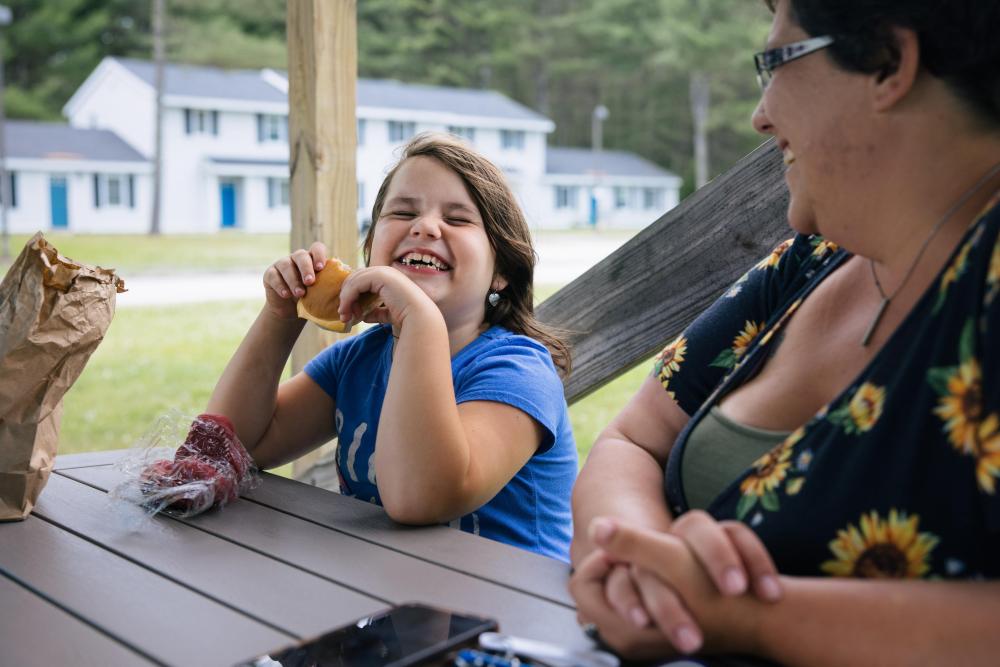 A girl eats food at a picnic table and laughs