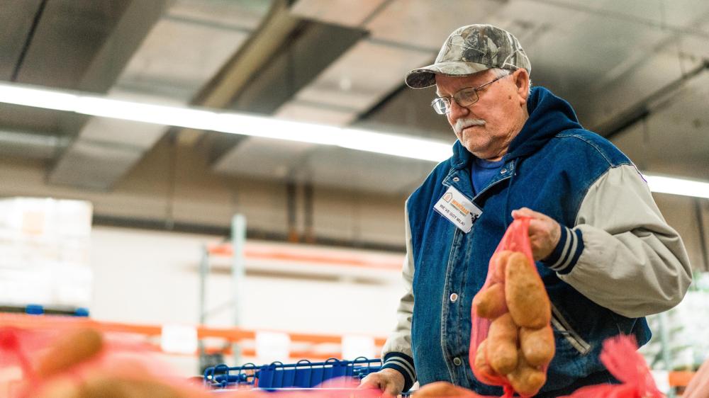 A senior man holds a bag of potatoes