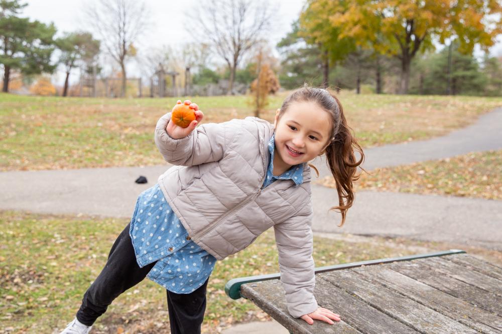 Child standing outdoors, holding a piece of fruit