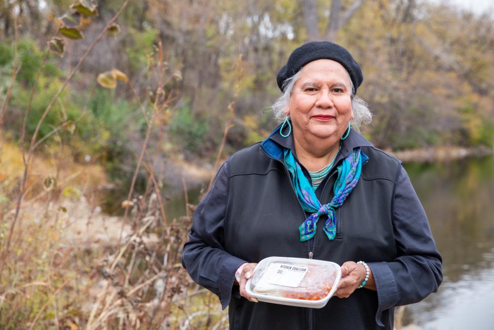 An elder standing outside, holding a prepared meal