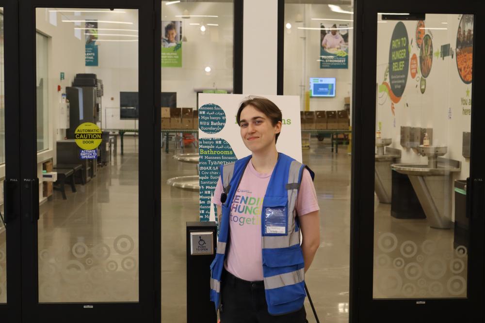 A person posing in front of a welcome center in a blue vest