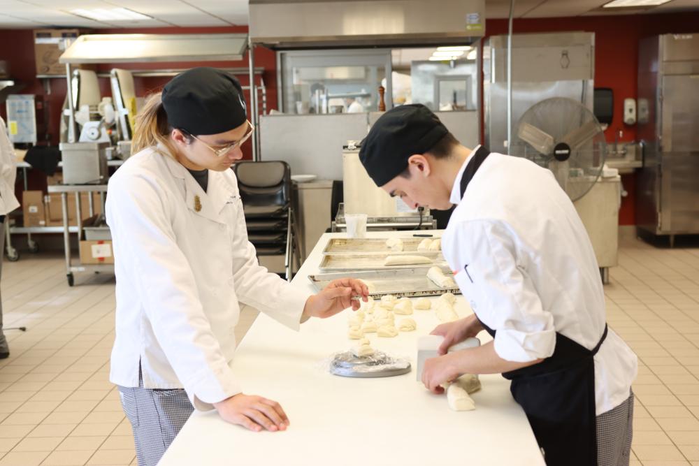 Two chefs cut bread dough in a kitchen