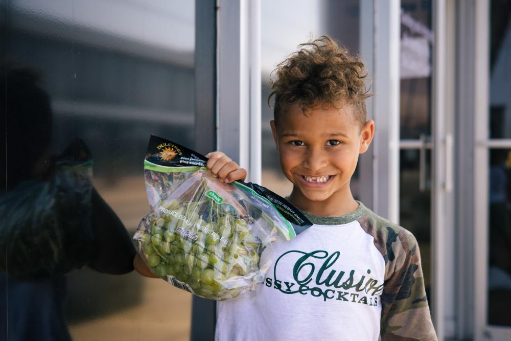 Young child, holding bag of grapes and smiling