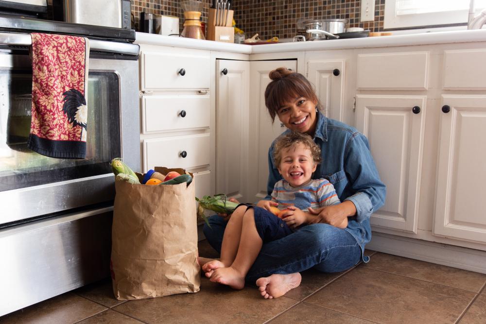 Mother and child, sitting on a kitchen floor next to a bag of groceries