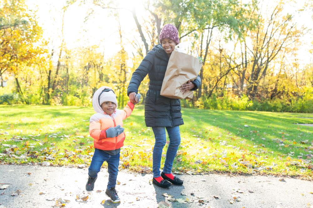 A mother and child walking outdoors with a bag of groceries