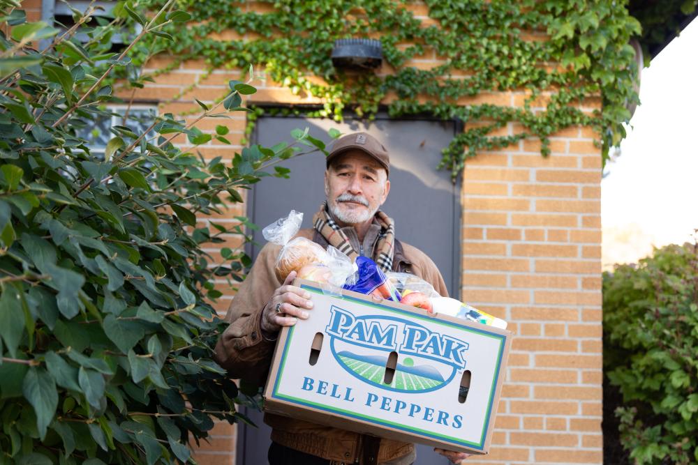 A man standing outside, holding a box of produce