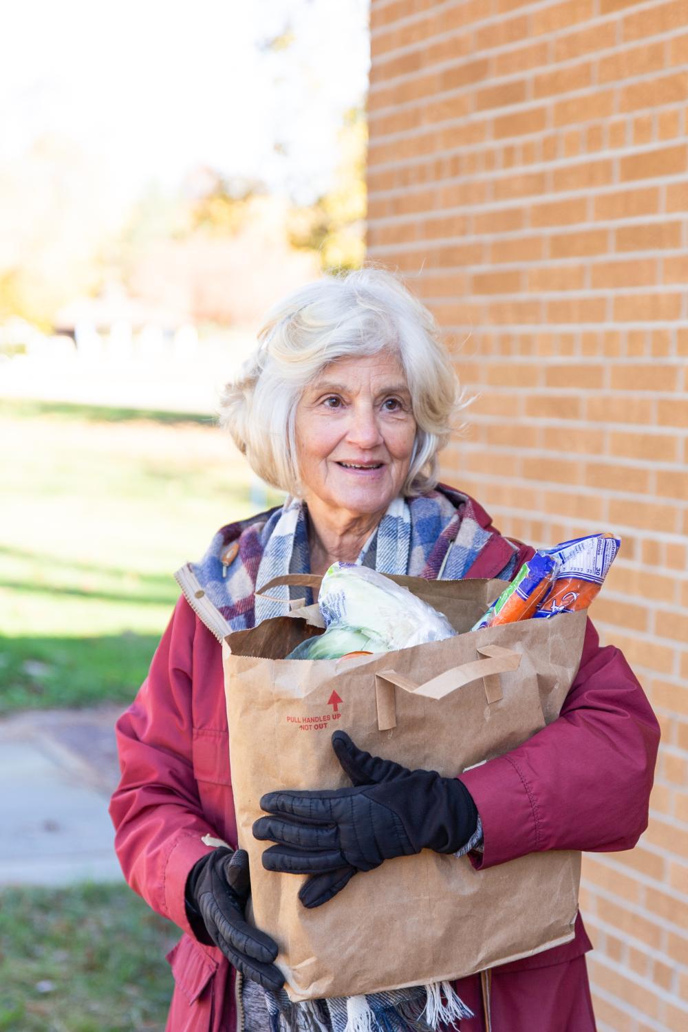 An elderly woman standing outside, holding a bag of groceries