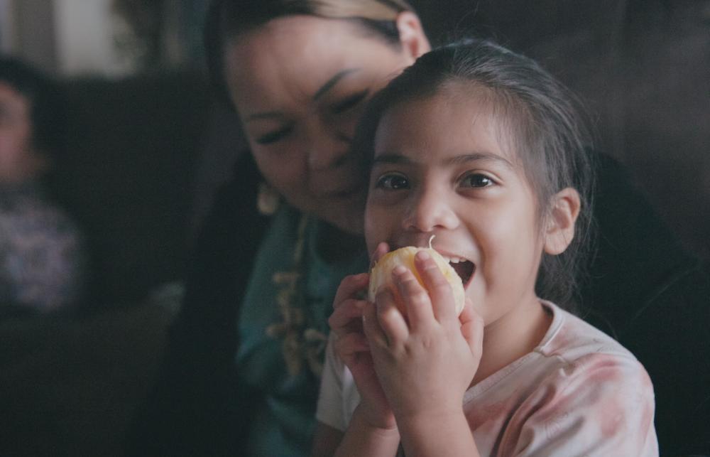 A child sitting with an adult, eating an orange