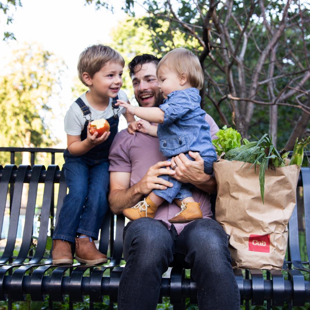 Parent and children on an outdoor bench with groceries