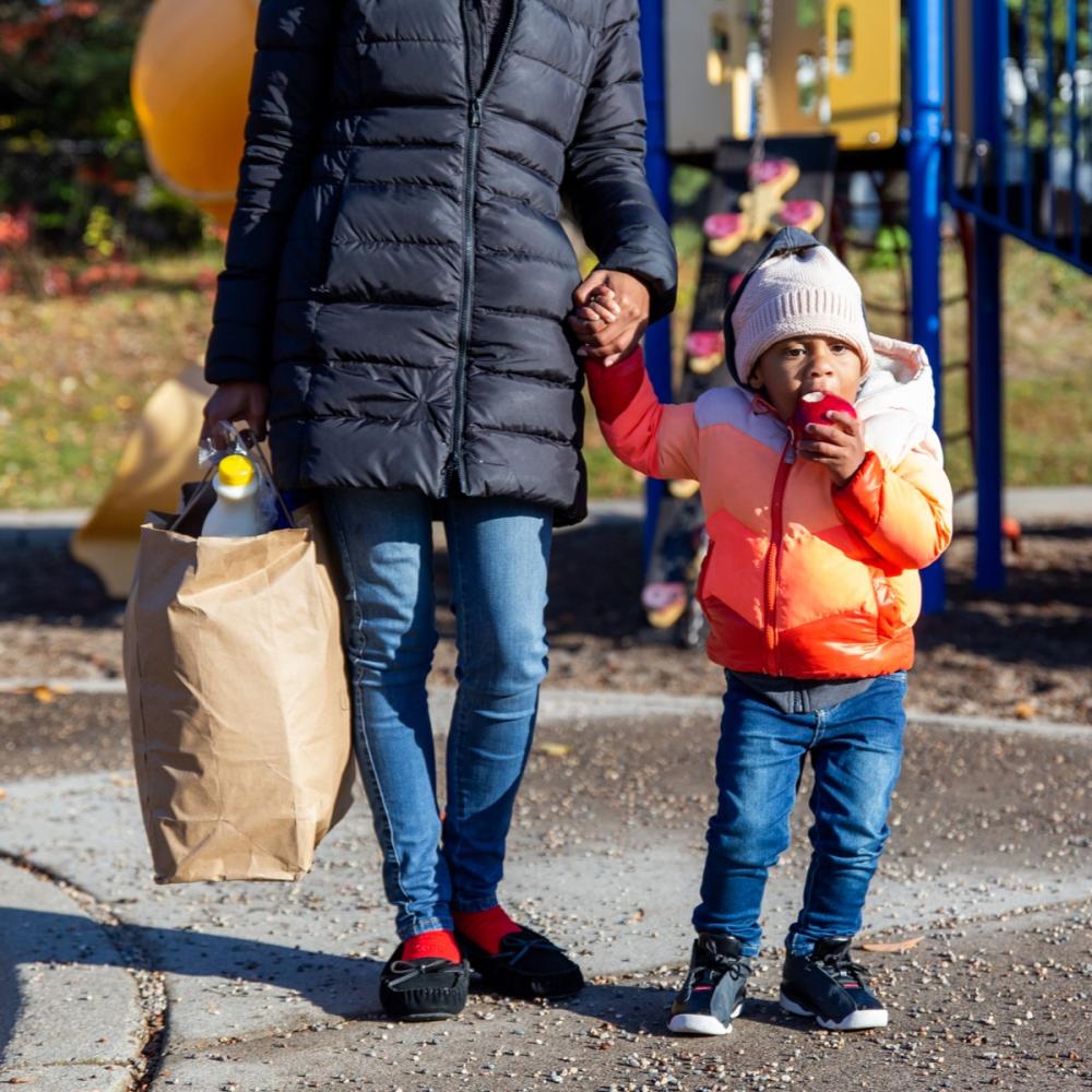 A parent and child standing outdoors with groceries