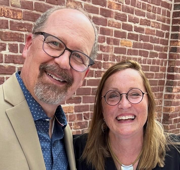 A couple smiles in front of a brick wall