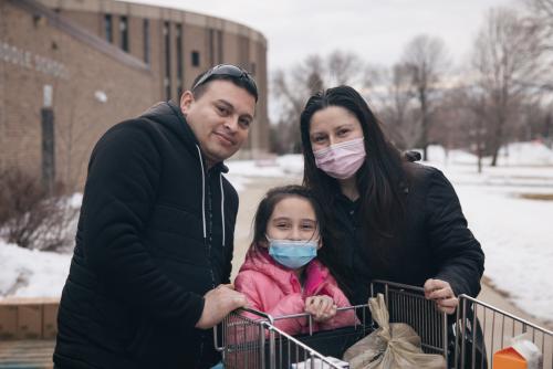 A family of three smiles at the camera after visiting an outdoor food distribution