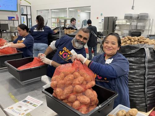 Two volunteers smiling at the camera while packing potatoes in the volunteer center.